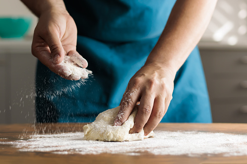 Unrecognisable man kneading by hand in kitchen, on wooden table. Spreading flour