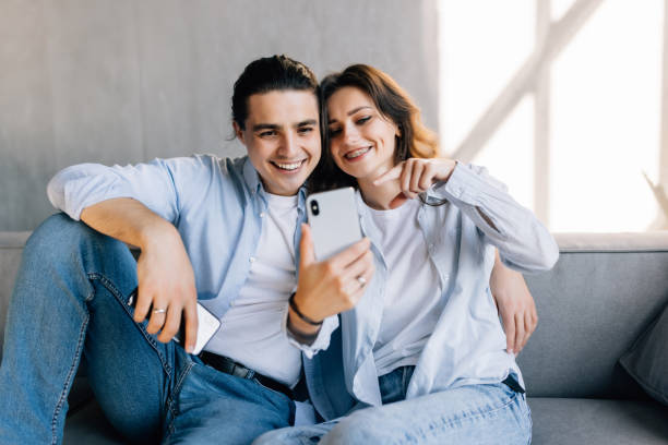 istock Young couple relaxing on a couch at home, hugging, taking a selfie 1454857448