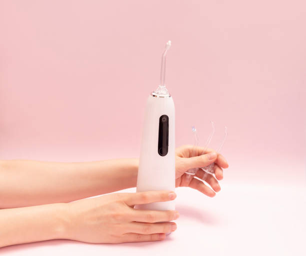 Hands hold oral teeth irrigator with nozzle pack, dental water tooth cleaner, white portable cordless water dental flosser on pink background. Waterproof home dental care device. Copyspace, horizontal Dentists recommend taking care of teeth cavity using Dental Water Teeth Cleaner Water Flossing. Professional teeth cleaning at home, portable water jet teeth cleaner. Mobile device for brushing your teeth and a snow-white smile. Space for text deep pick stock pictures, royalty-free photos & images