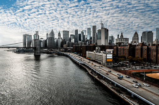 Lower Manhattan, highway and a part of the Brooklyn Bridge seen from the Manhattan bridge during a rush hour and an amazing sunset making a cloudy sky so impressive.