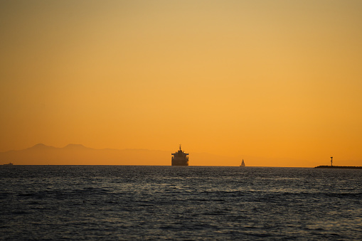 Industrial Container or Tanker Ship on Calm Seas with a Sailboat close by on a beautiful clear sunset near Los Angeles in the Pacific Ocean
