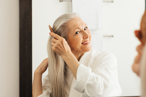 Senior woman in her 60s with grey bobbed hair, smiling at the camera. She looks content and relaxed, in front of a grey background.