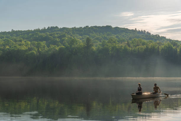 Couple canoeing on a lake of the Laurentians,  Quebec, during a sunrise of summer.