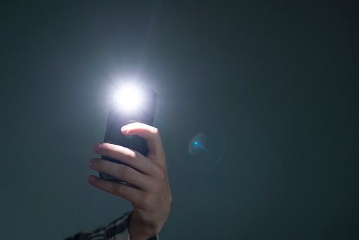 Mano sosteniendo un teléfono inteligente utilizado como una linterna incendiada, de teléfono móvil en la oscuridad photo