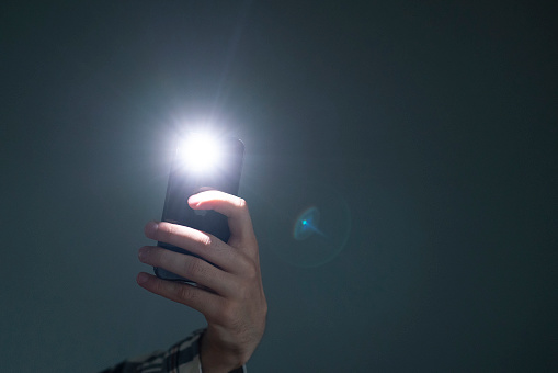 hand holding a smartphone used as a torched, flashlight of mobile phone in the dark