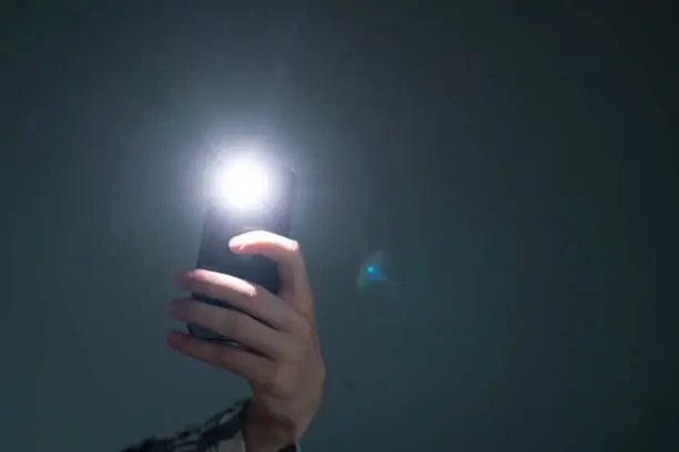 Photo of hand holding a smartphone used as a torched, flashlight of mobile phone in the dark