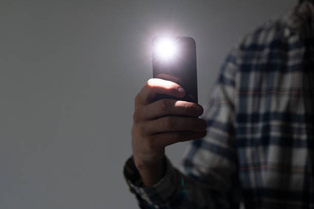 istock hand holding a smartphone used as a torched, flashlight of mobile phone in the dark 1454877231