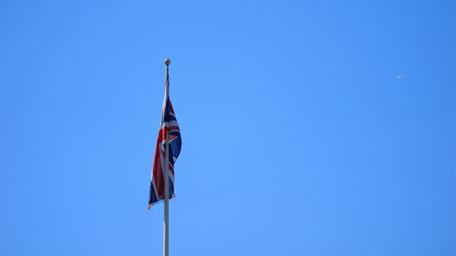 The big national flag of the United Kingdom. British flag flying in the wind, in the sun. Slow Motion. Aircraft in the background. 4k Version 2