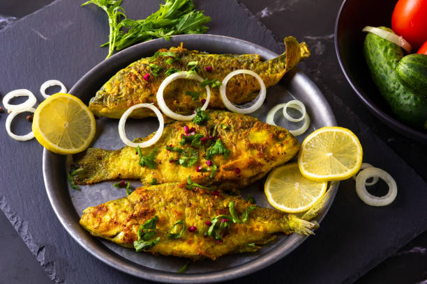 istock Fried Freshwater Fish with Lemon in a Plate on Black Slate Board. 1454882575