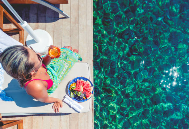 istock Woman drinking and Aperol Sritz sitting on a deck chair on a deck by the ocean. 1454884737