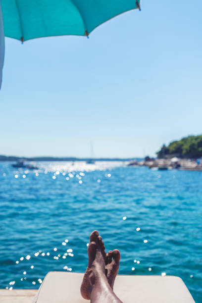 Man lying by the ocean on a deck chair. Only his feet can be seen with the ocean in the background.