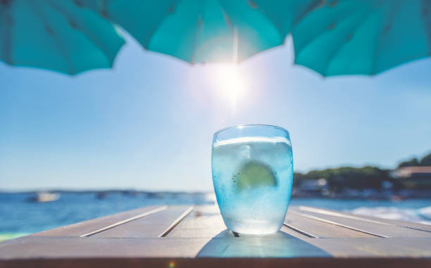 Glass of Water at the beach. Lemon and ice in the blue glasses. Backlit at sunset.