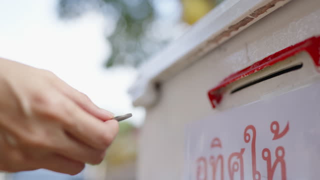 A person is donating a coin to the donation box that is set up around the temple in Chiang Mai Thailand
