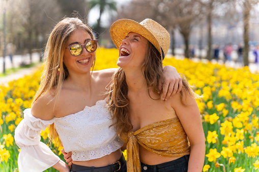 A closeup of two beautiful laughing girls standing against the background of yellow flowers.