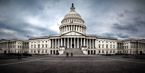 Panoramic view of rear facade of Capitol building in Washington, D.C. on a cloudy and moody day. Some tourist passing in front of it.
