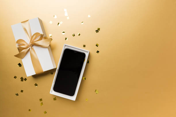 istock Opened gift box with gold ribbon and smartphone on color background, top view. Blank open box packaging mockup , Template for your design - branding mockup 1454894281