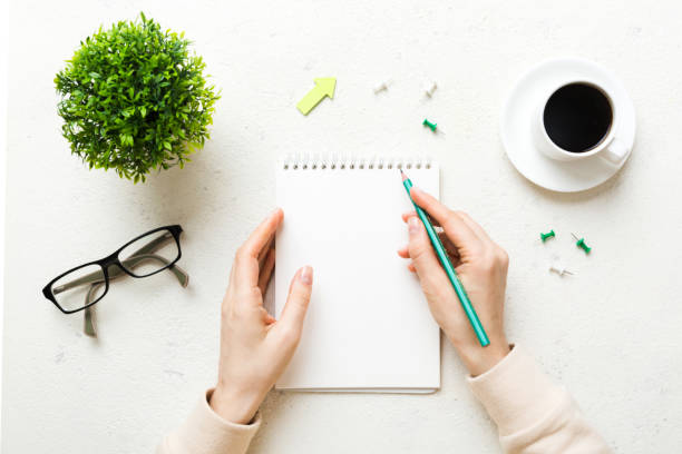 istock Woman hand with pencil writing on notebook and hold coffee cup. Woman working on office table with coffee 1454894361