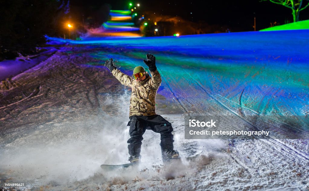 A snowboarder in action illuminated at night with colorful lights behind A night action shot of a snowboarder making a turn. Illuminated with flash and colorful lights behind. Iwate Prefecture Stock Photo