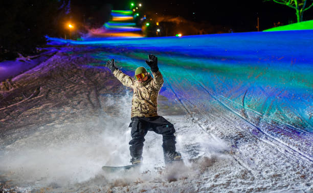 A snowboarder in action illuminated at night with colorful lights behind A night action shot of a snowboarder making a turn. Illuminated with flash and colorful lights behind. japanese snowboarder stock pictures, royalty-free photos & images