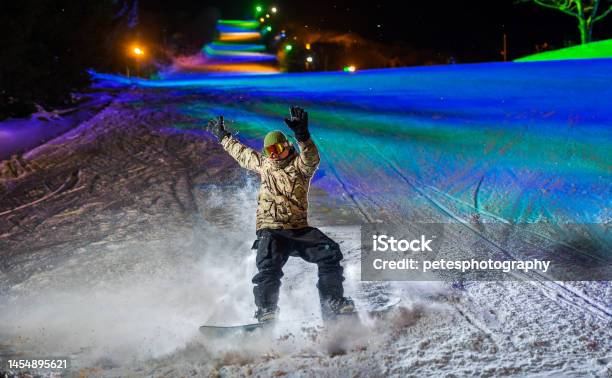 A Snowboarder In Action Illuminated At Night With Colorful Lights Behind Stock Photo - Download Image Now