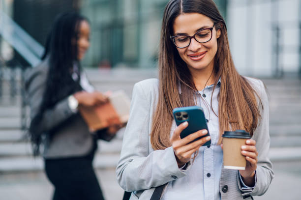 istock Business woman standing outside while using a smartphone and drinking coffee 1454895833