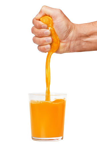 A man's hand squeezes a ripe orange into a glass. A man is holding and squeezing an orange. Orange juice is pouring. Isolated on a white background.