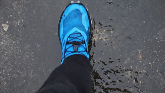 View of shoes wading in a puddle, the water spilling out at a slow motion.