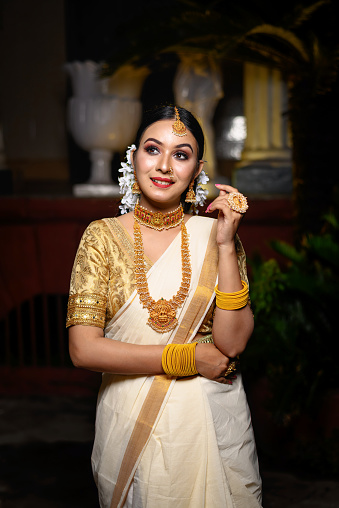 Magnificent young Indian bride in luxurious bridal costume with makeup and heavy jewellery standing in front of a vintage background. Lifestyle and Fashion. Ethnic wedding and fashion.