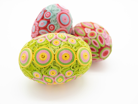 Close up of three quill art Easter eggs against a white background. The eggs are lime green, pink, yellow, and fuchsia.
