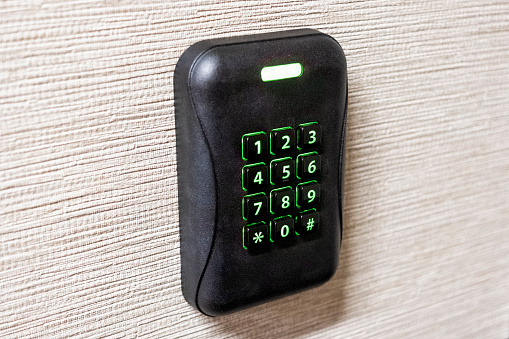 A side view angle close up photograph of a black security system keypad with numbers illuminated in green.
