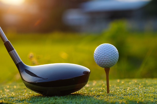 Golf clubs and golf balls on a green lawn in a beautiful golf course with morning sunshine.