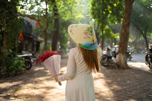 Portrait of Asian with bouquet flowers, Vietnamese woman girl traveling in Hanoi urban city town, Vietnam. People lifestyle.