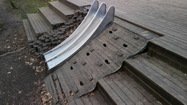 double shiny stainless steel slide on the playground. a hill lined with wooden logs used as palisades. autumn day park. it resembles a rocky slope, palisade, palissade, slope, hill, terrace, above, retaning tobogán doble brillante de acero inoxidable en el patio de recreo. una colina bordeada de troncos de madera utilizados como empalizadas. parque de día de otoño. se asemeja a una pendiente rocosa, empalizada, empalizada, pendiente, colina, terraza, arrib