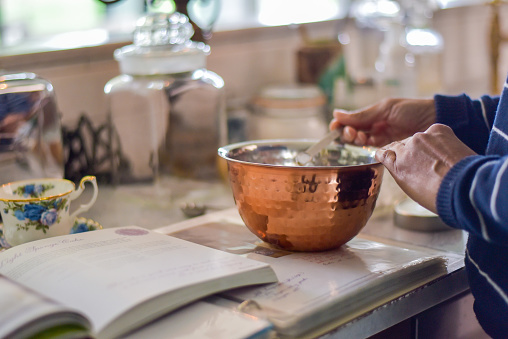 woman measuring out dry baking ingredients in a copper bowl.