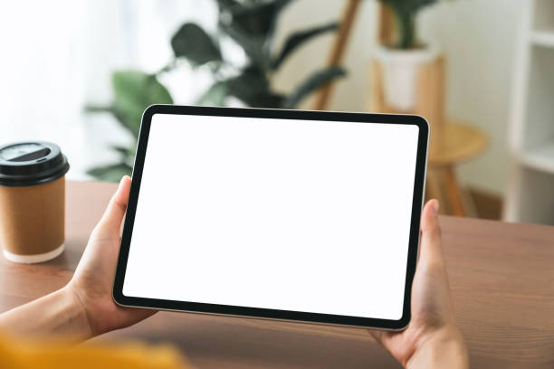 manos sosteniendo la tableta digital con maqueta de pantalla en blanco en el sofá de la sala de estar. - new ipad fotografías e imágenes de stock