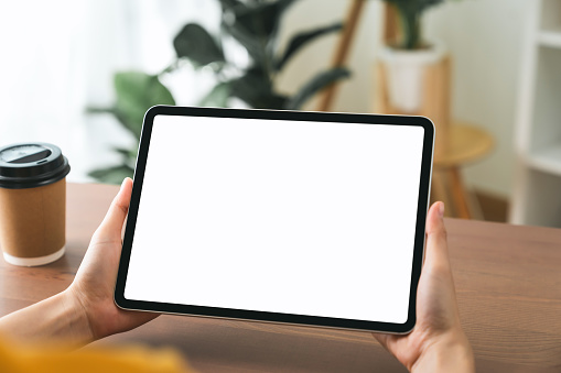 Hands holding digital tablet with mockup of blank screen on sofa in living room.