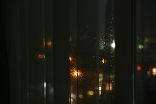 raindrops on the window at night, view through transparent window curtains, blurred abstract background with night city lights