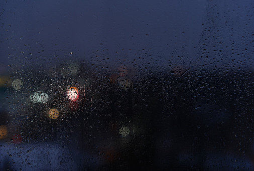 Raindrops on a window glass and unfocused lights of a evening city. Background of night city behind glass during rain, copy space