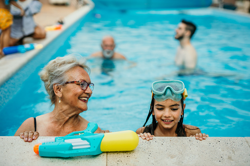 Happy family having fun in the swimming pool. Focus on a girl and her grandmother playing in the pool.