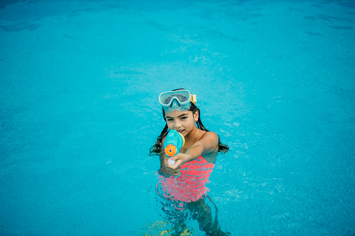 Happy little girl playing with water toys on a hot summer day. The little girl in the pool having fun by herself. She is wearing goggles.