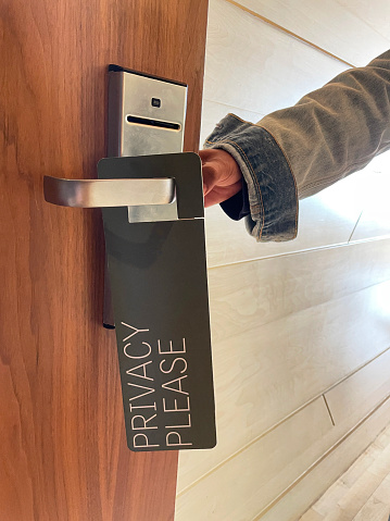 Stock photo showing a 'Privacy Please' sign hanging from the handle of a hotel room door that has been opened by an unrecognisable person.