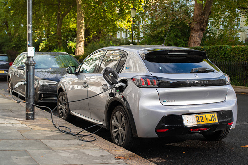 London, UK - October 01 2022: Silver Peugeot e208 in Kensington on a sunny autumn day. Electric car on charging spot in a big city.