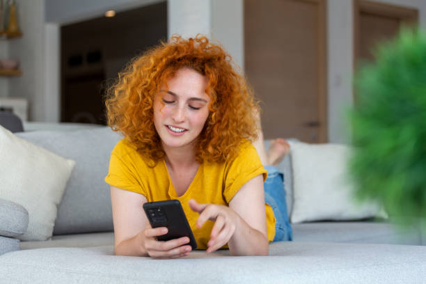 istock Woman using mobile phone while lying on sofa. Young female is resting at home. 1454954061