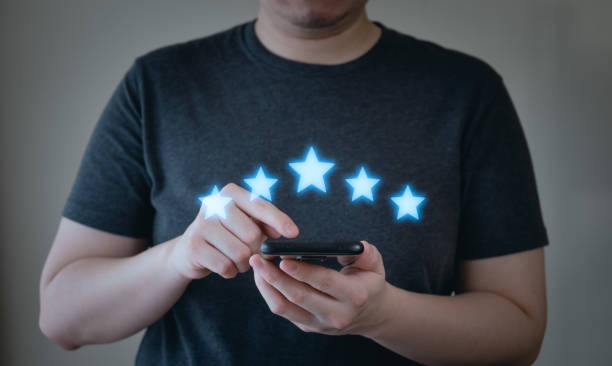 istock Close up of customer using mobile phone with five stars best rating feedback icon. Customer service satisfaction evaluation concept. 1454955368