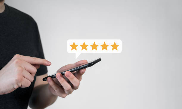 istock Close up of customer using mobile phone with five stars best rating feedback icon. Customer service satisfaction evaluation concept. 1454955378