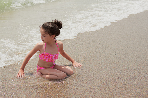 Girl in a pink bikini playing happily on the shore of the beach with the waves on a sunny summer day, Vera, Spain