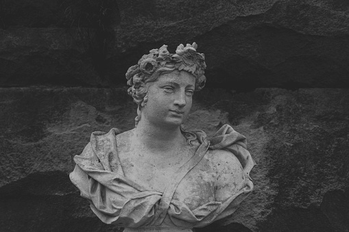 A grayscale shot of a historical woman's sculpture built on an old rocky wall