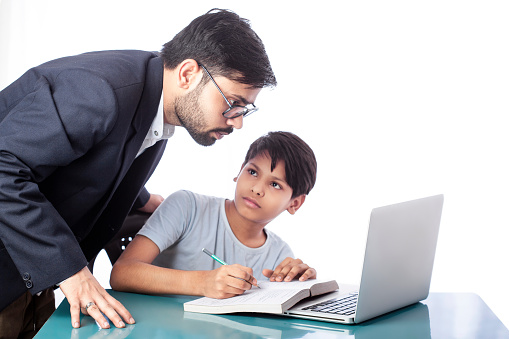handsome father helping son in his study in front of a laptop and books on desk