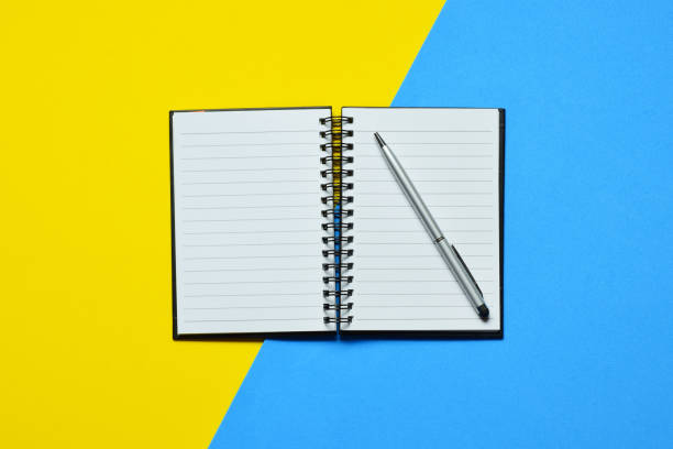 istock Top view of an open notebook with a pen on it on two-toned blue and yellow background 1454962439
