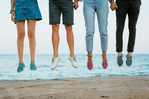 A closeup of a group of young people jumping for joy against the sea.